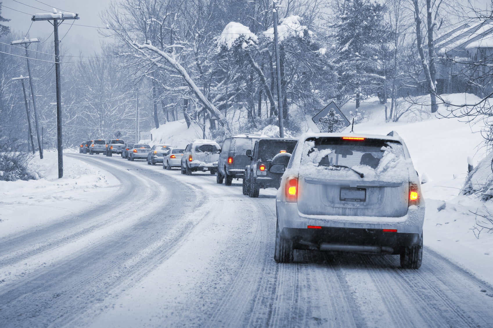 A line of vechicles driving down a snow covered road.